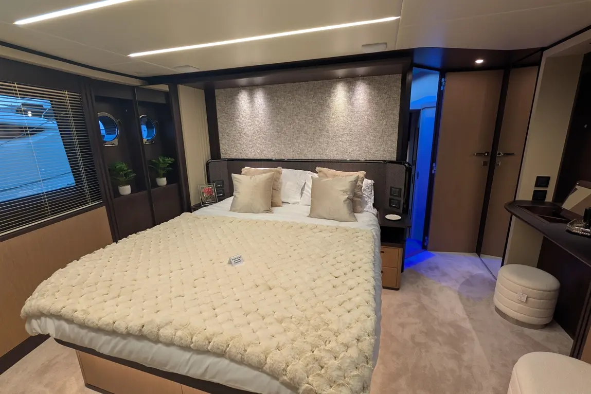 Luxury bedroom with a plush bedspread, decorative cushions, mirrors, potted plants, and ambient lighting in a boat cabin.
